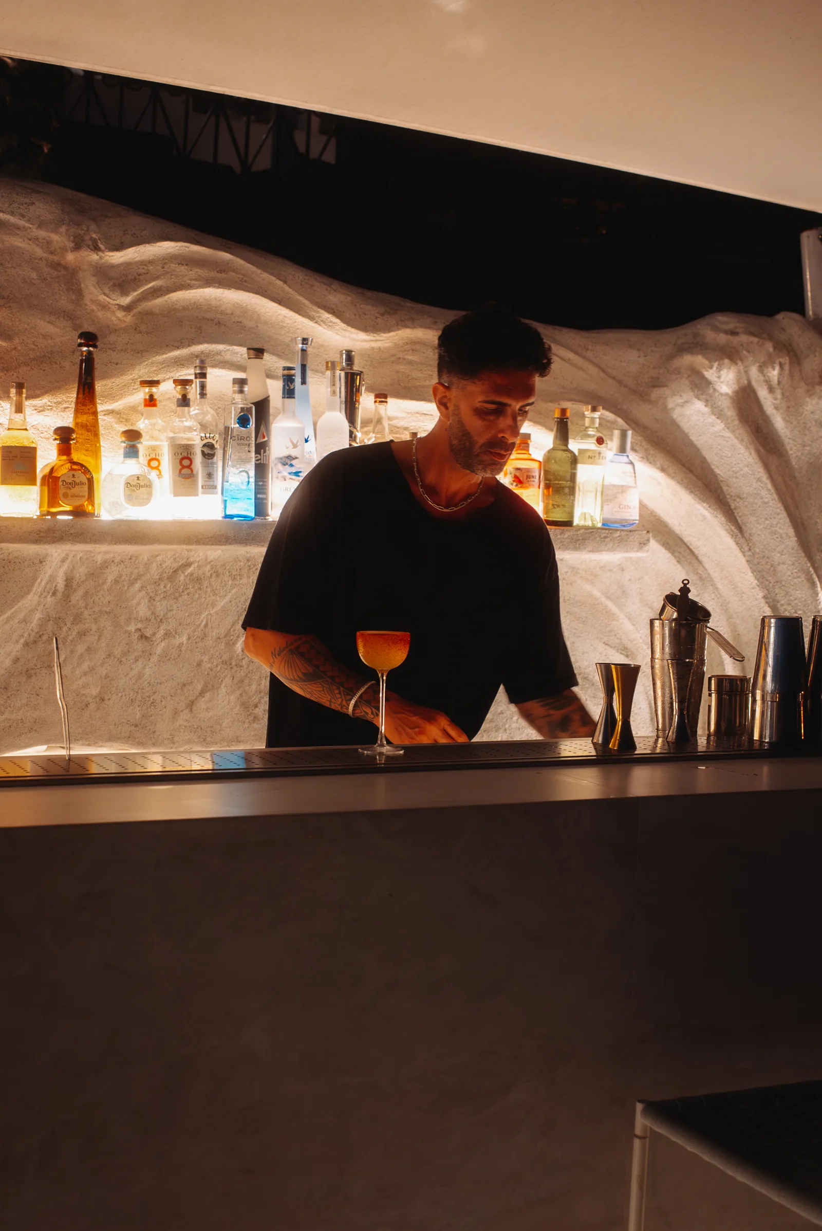 A bartender setting a finished coupe down on the lit cave-bar counter.