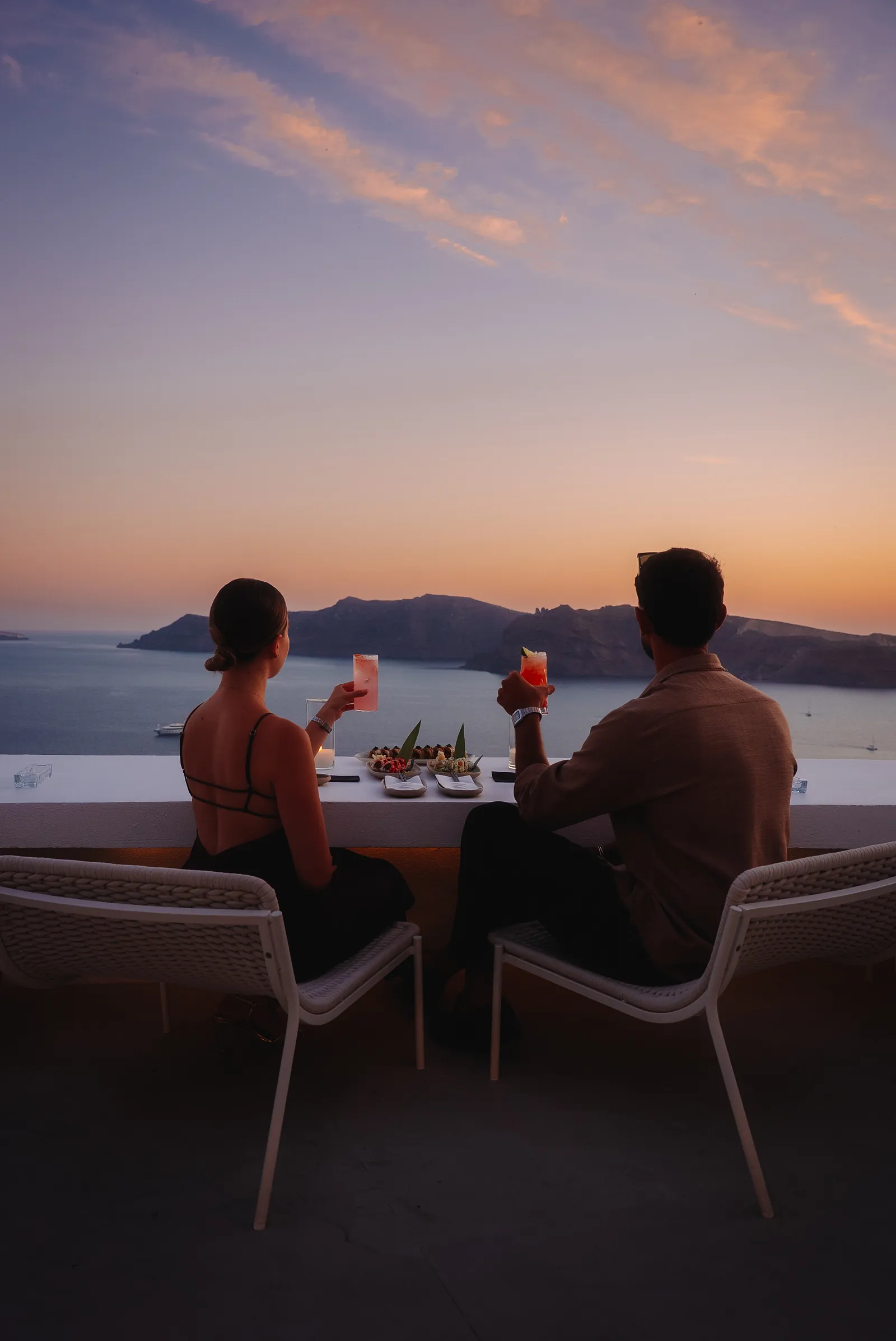 A couple at the rooftop rail as the sun drops behind the caldera.