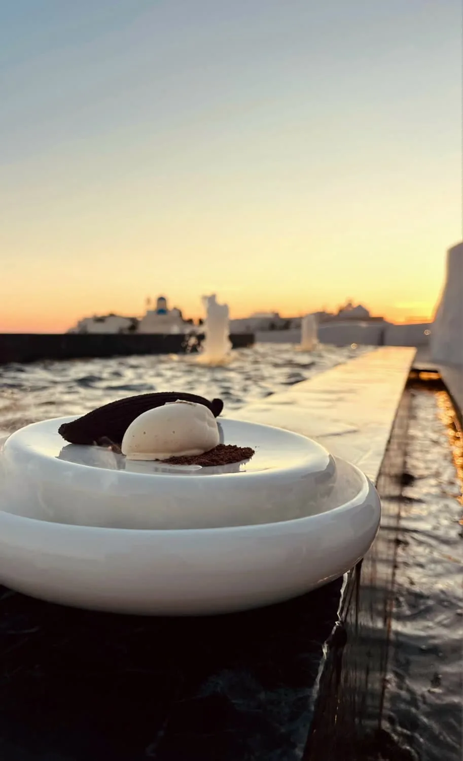 A dessert plated at the pool edge as the sun drops behind Oia.
