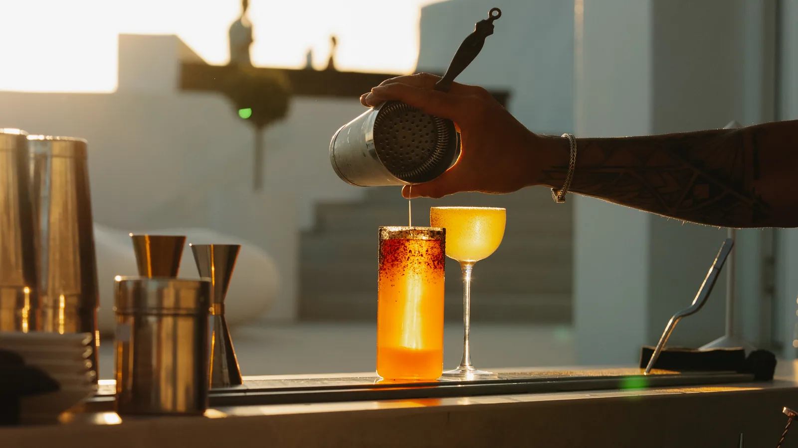 A cocktail poured out at the bar in low golden light, a coupe beside it