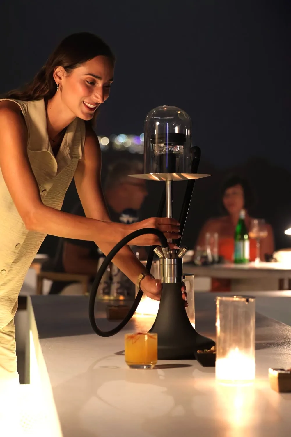 A shisha being prepared at the table, guests talking behind.